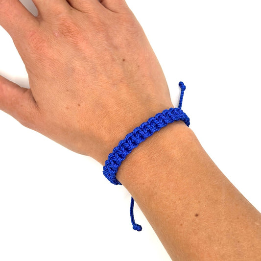 Handgelenk einer Frau mit einem geknüpften Armband. Das Armband ist metallic blau und mit einem Kreuzknoten gknüpft
