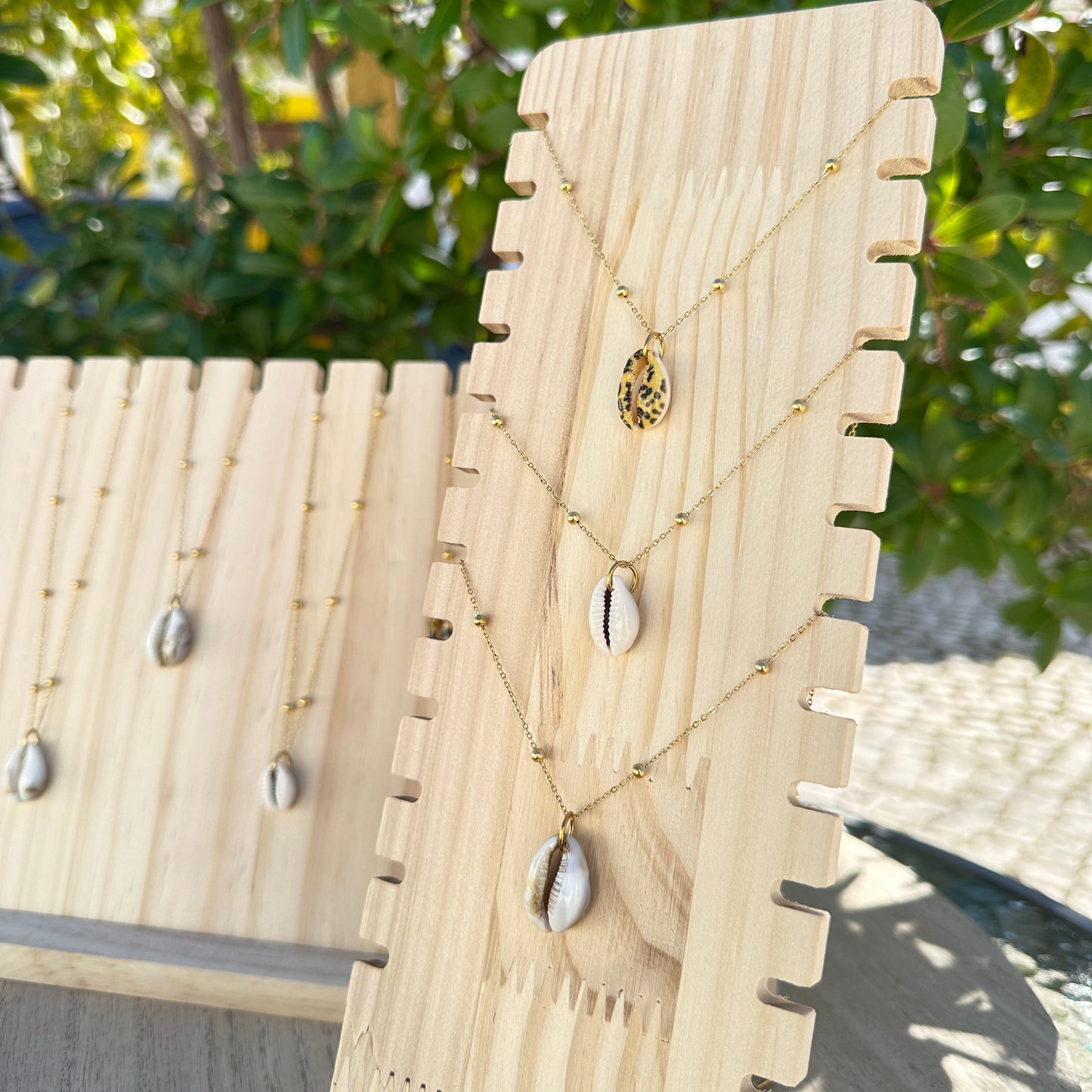 Gesamtes Sortiment der Kaurimuschel-Halsketten in verschiedenen Varianten auf Holzdisplay.