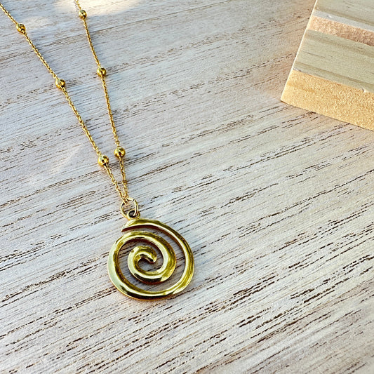 Goldene Halskette mit Spiral-Anhänger aus Edelstahl, flachliegend auf hellem Holz fotografiert