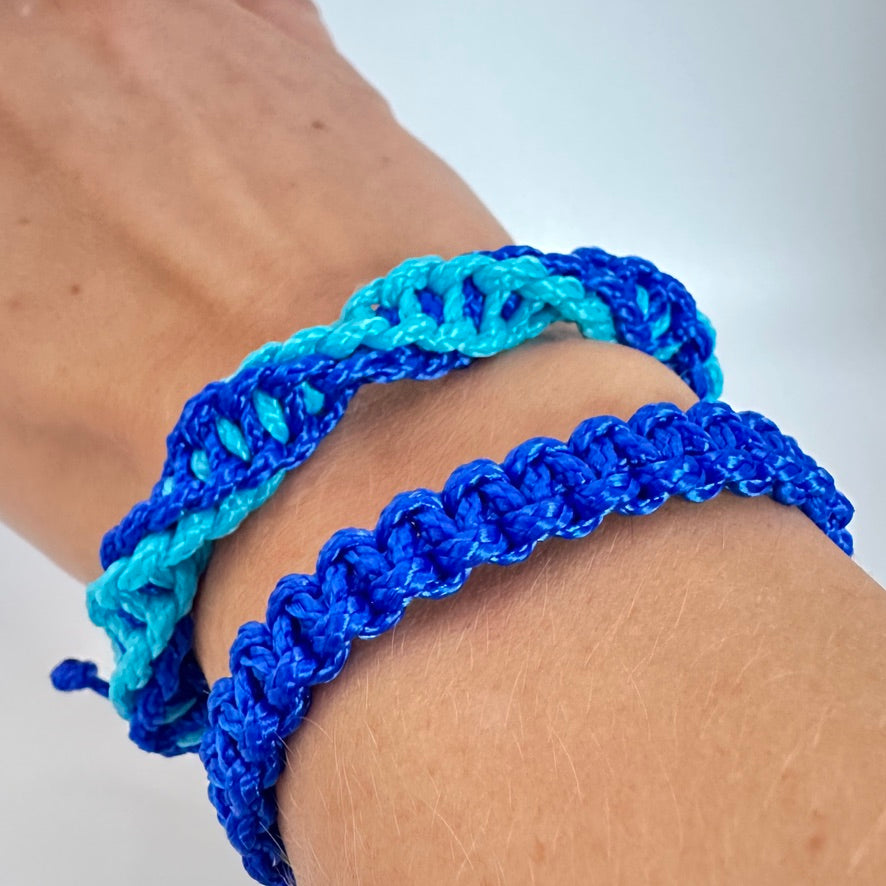 Handgelenk mit 2 Armbändern aus PPM-Schnur. Ein Blaues Armband geknüpft mit Kreuzknoten, ein zweites im gedrehten Kreuzknoten mit zwei Farben: blau und türkis