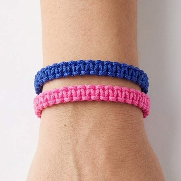Handgelenk mit zwei Makramee Armbändern. Ein Armband ist blau, das andere Neon-Pink. Geknüpft mit dem Kreuzknoten
