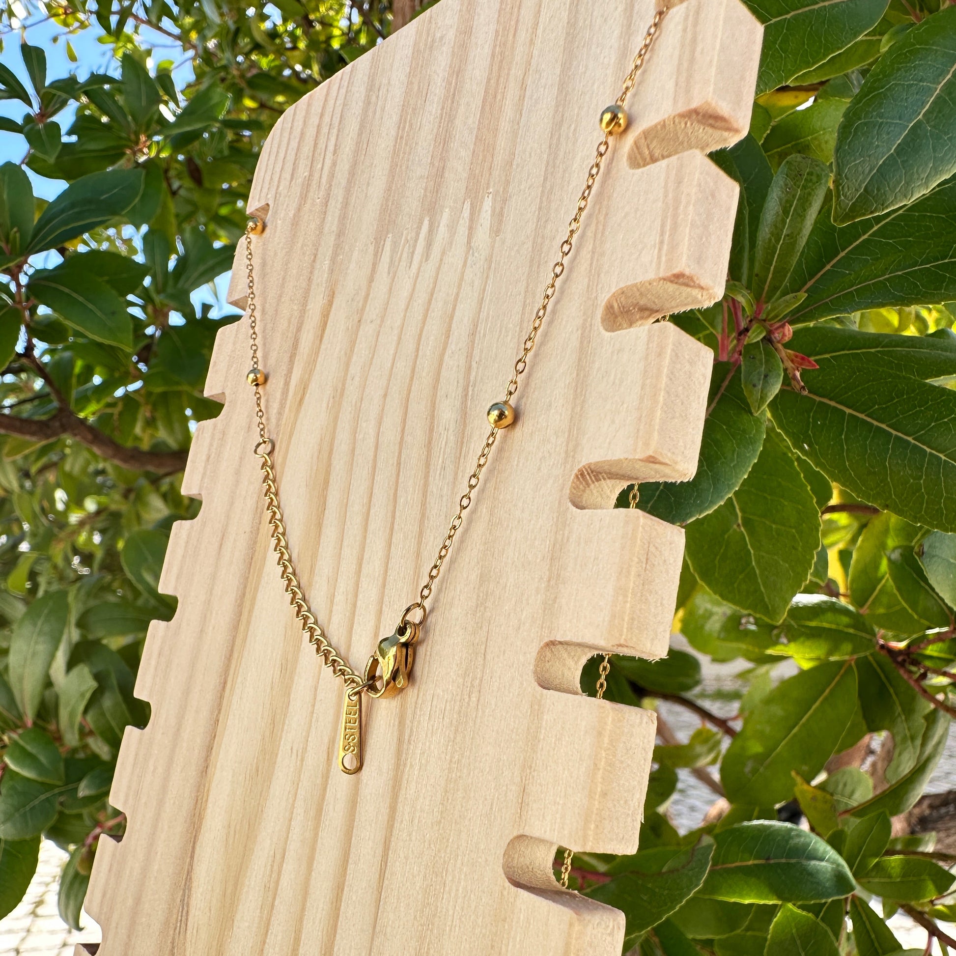 Rückansicht einer goldfarbenen Edelstahlkette mit Karabinerverschluss und Verlängerungskette auf Holzdisplay im Außenbereich.