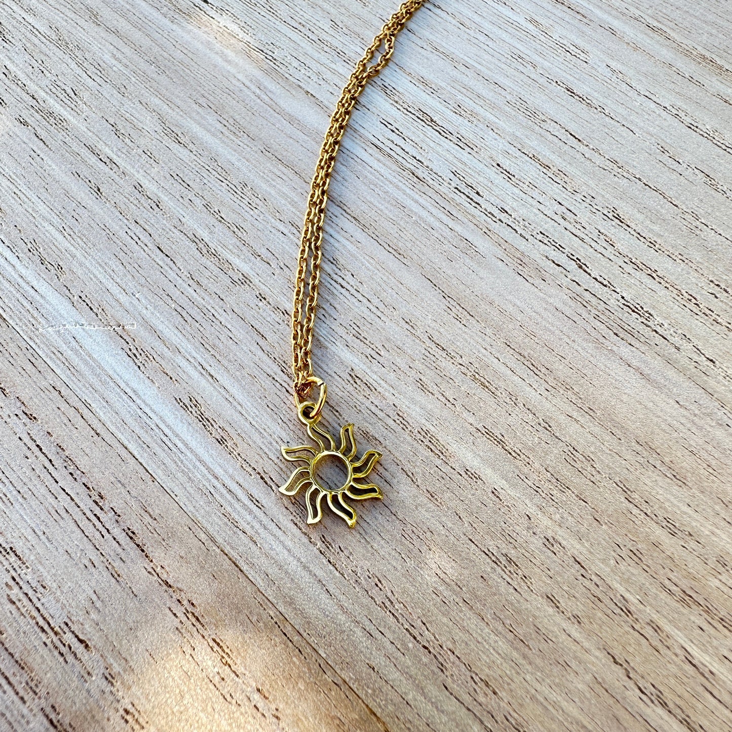 Zarte goldfarbene Sonnen Kette aus Edelstahl auf hellem Untergrund.