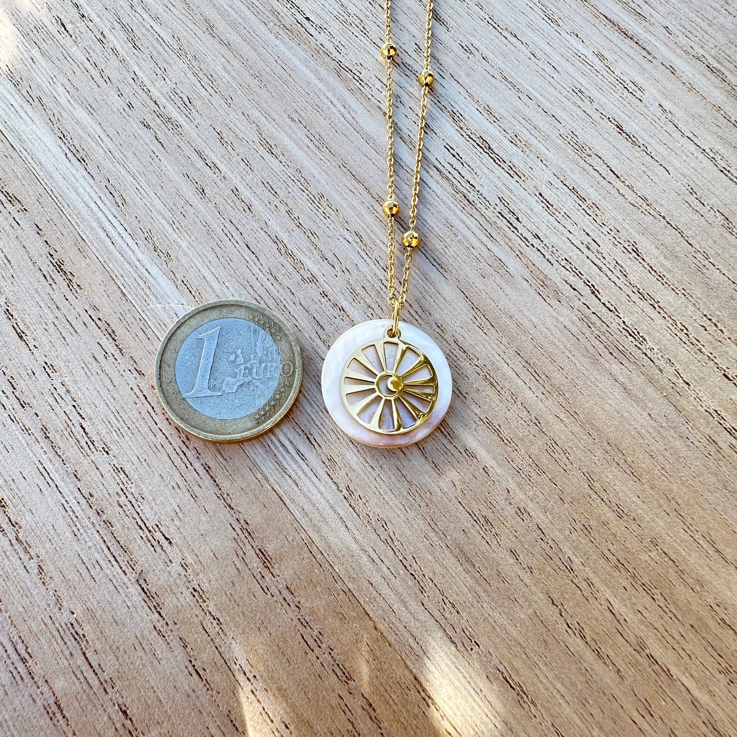 Goldfarbene Edelstahl Halskette mit rundem Perlmutt Sonne-Mond Anhänger neben einer 1-Euro-Münze zum Größenvergleich.
