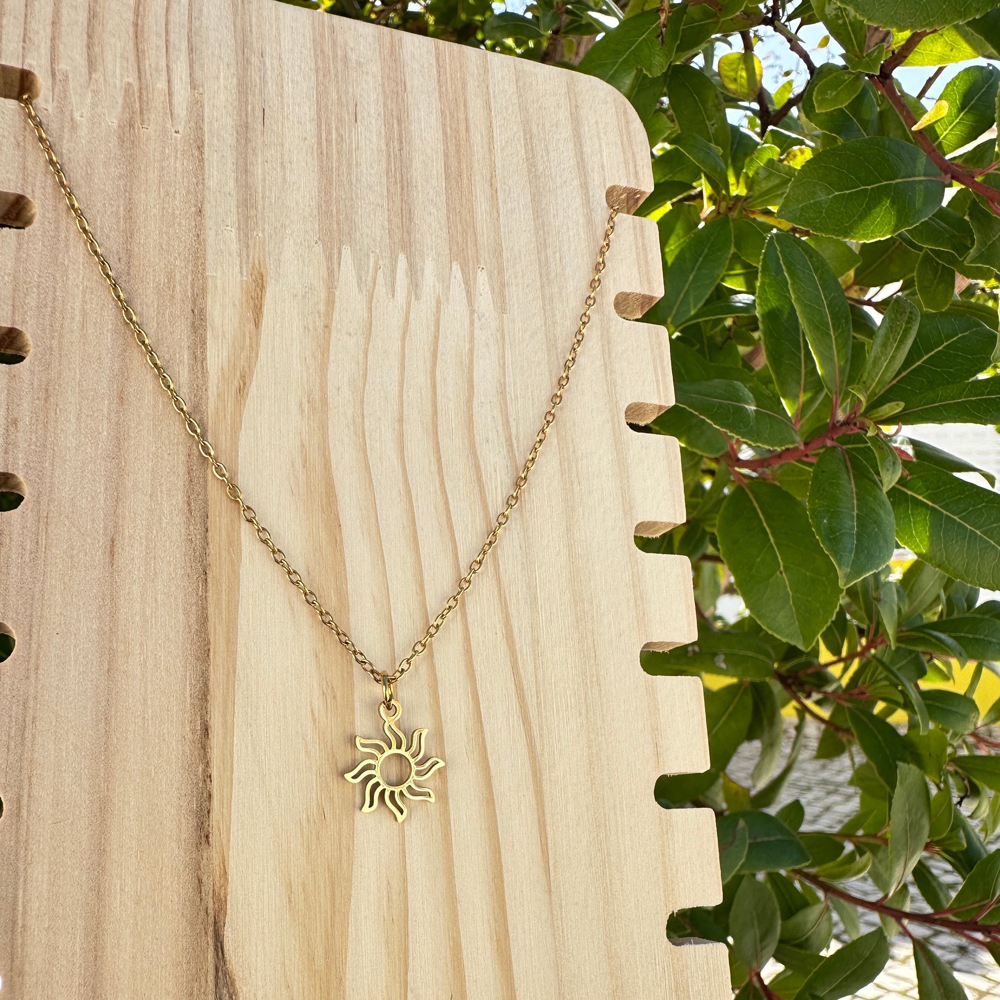 Filigrane goldene Halskette mit Sonnenanhänger aus Edelstahl auf hellem Holz.