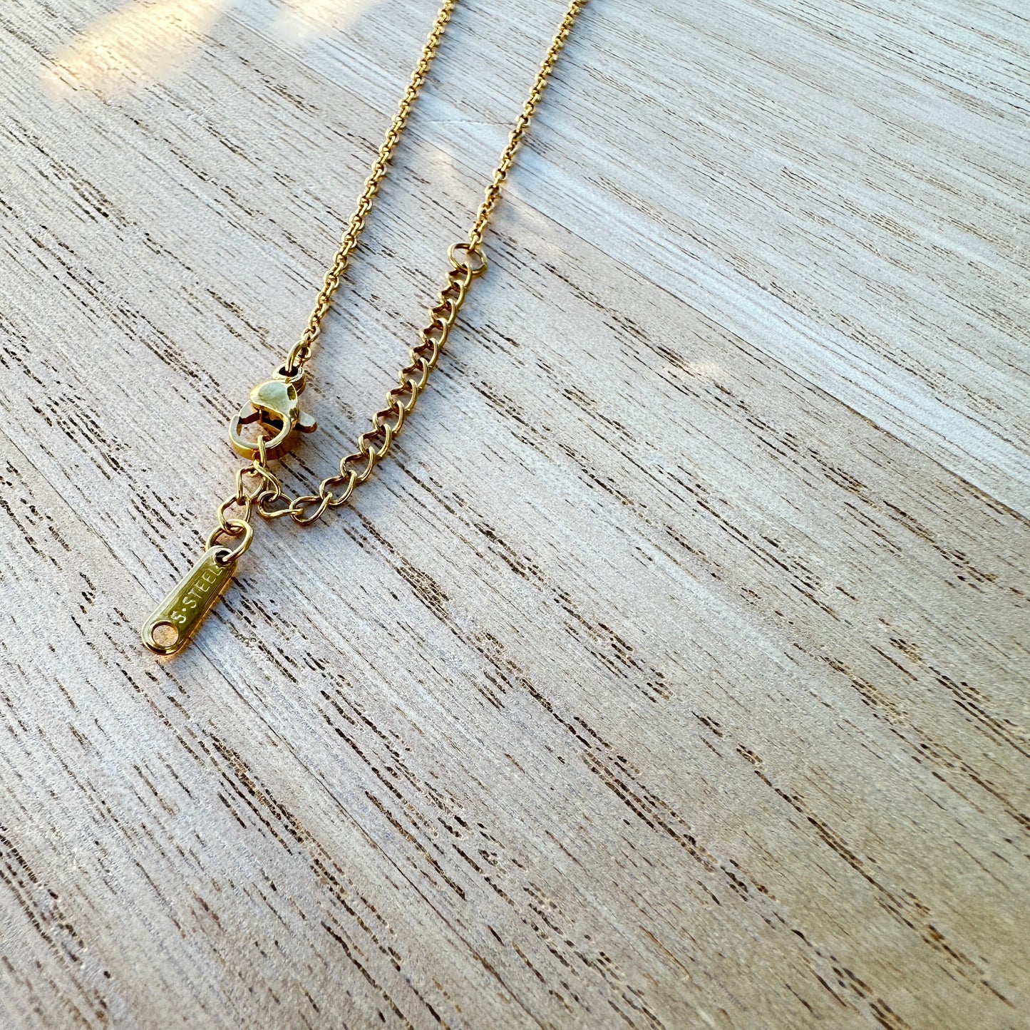 Detailaufnahme des Karabinerverschlusses einer goldfarbenen Edelstahl Halskette mit Palmen Anhänger und Verlängerungskette.