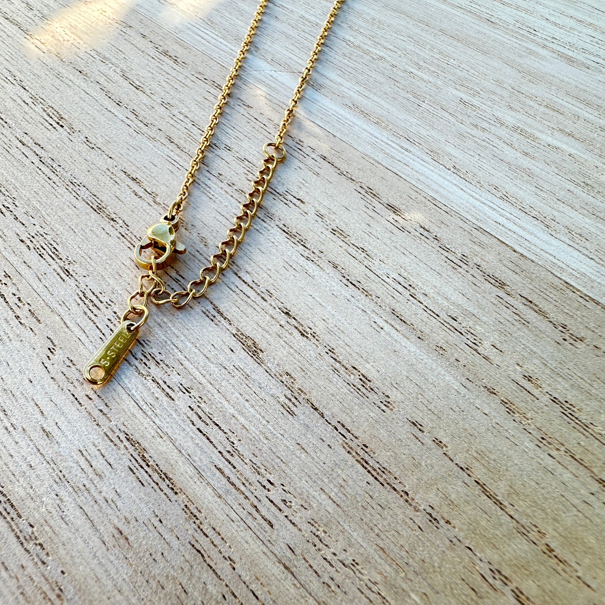 Detailaufnahme des Karabinerverschlusses einer goldfarbenen Edelstahl Halskette mit Palmen Anhänger und Verlängerungskette.