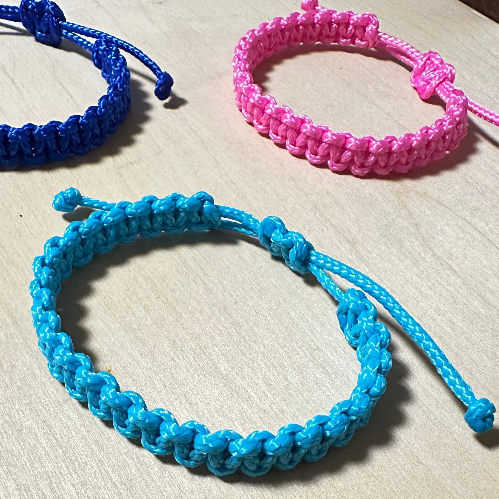Segeltau Armbänder in den 3 Farben türkis, neonpink und lau auf einer hellen Tischplatte. 