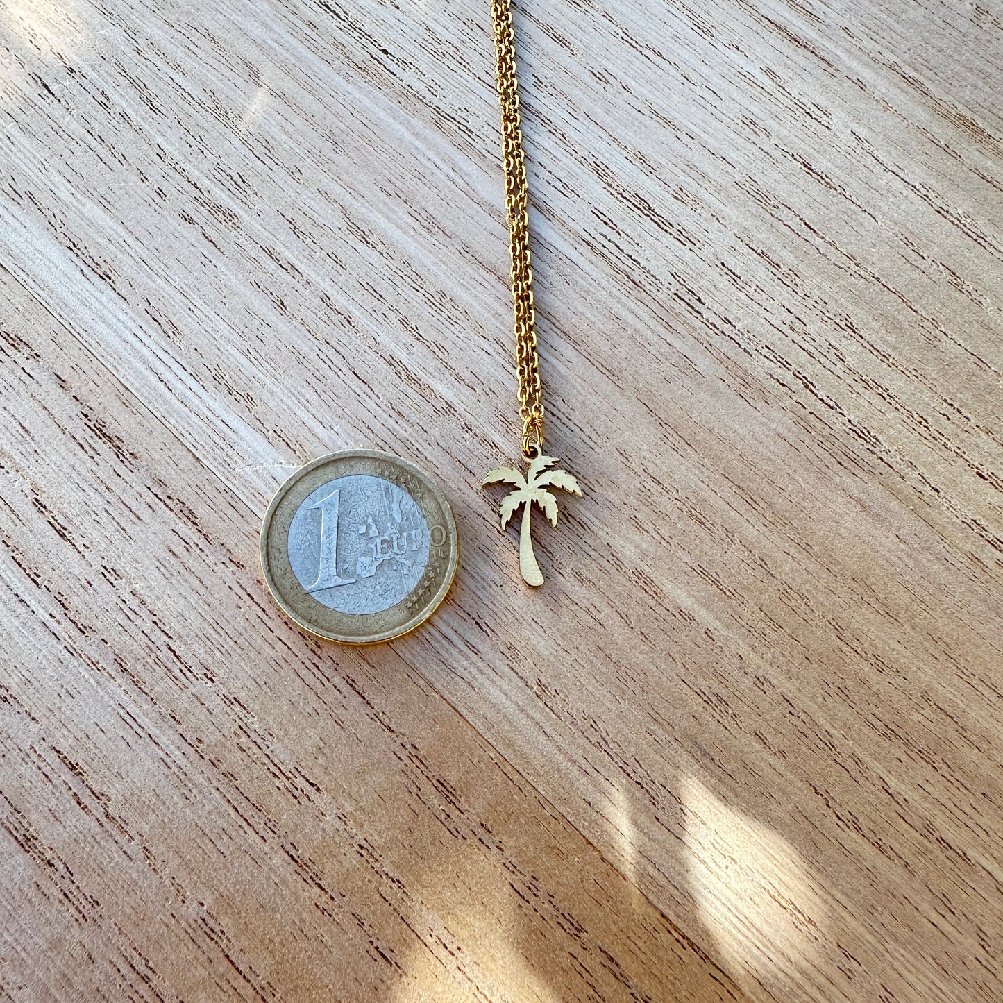 Goldfarbener Palmen Anhänger aus Edelstahl neben einer 1-Euro-Münze zum Größenvergleich.