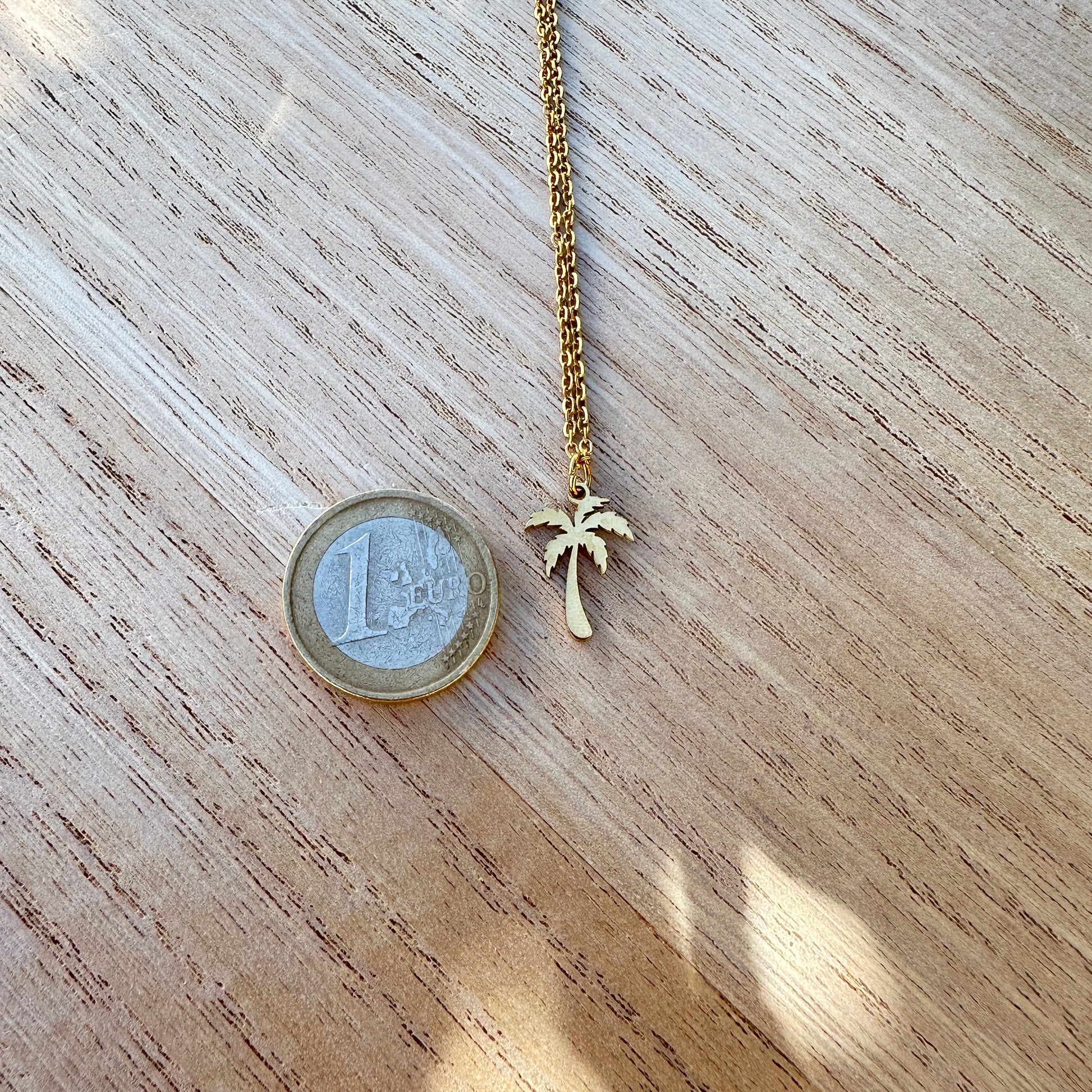 Goldfarbener Palmen Anhänger aus Edelstahl neben einer 1-Euro-Münze zum Größenvergleich.