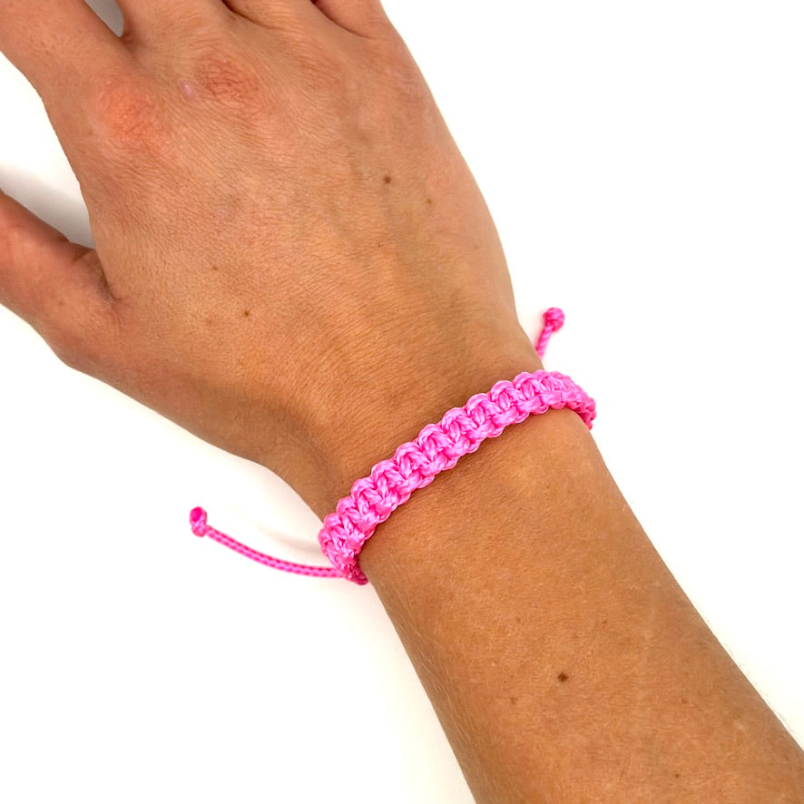 Handgelenk mit Neon-Pinkem Armband auf gebräunter Haut. Geknüpft mit einem Kreuzknoten.
