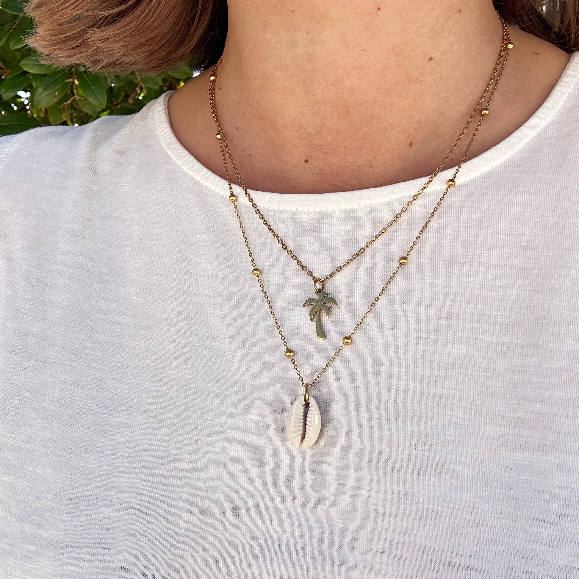 Weiße Kaurimuschel-Halskette kombiniert im Layering-Look mit goldener Kette.
