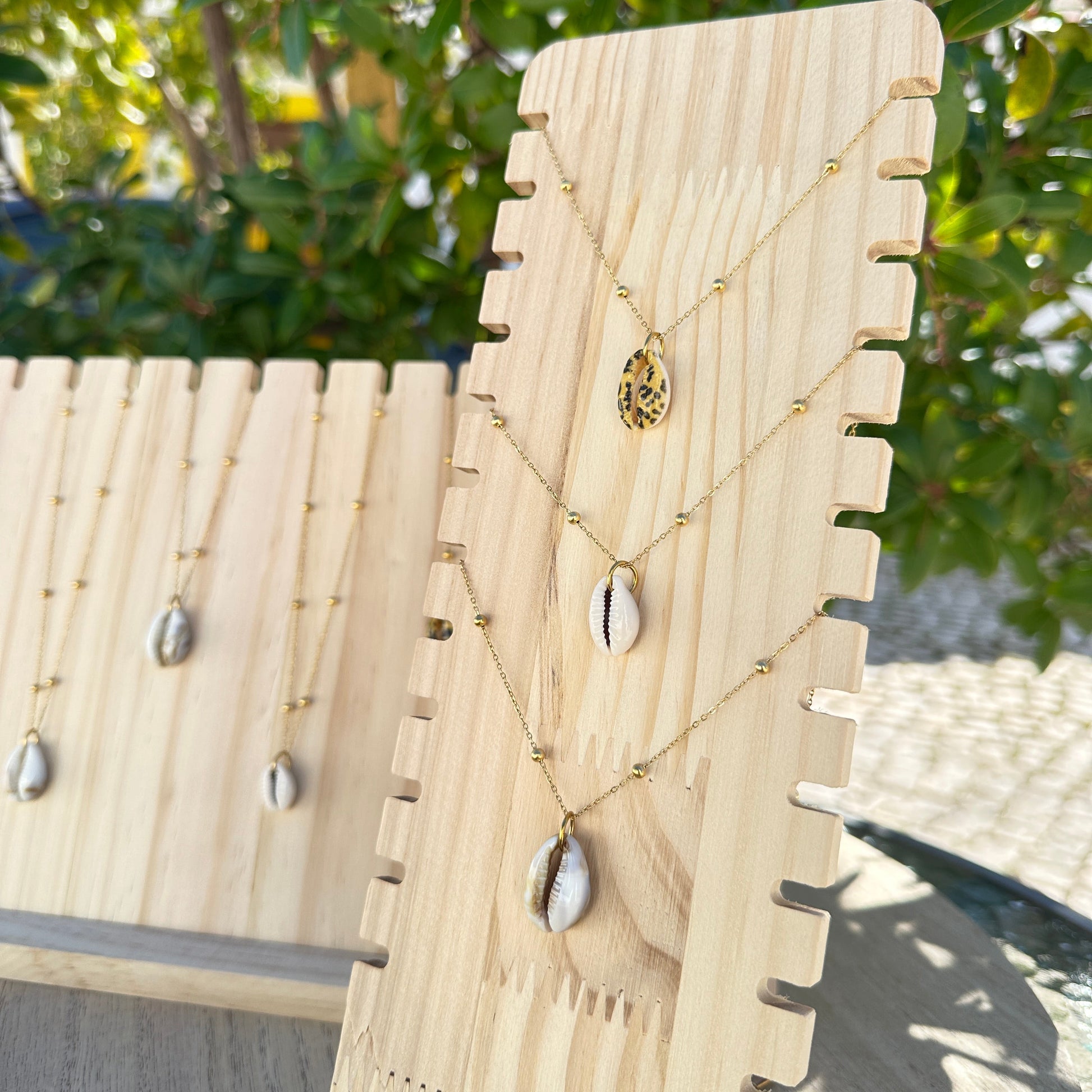 Gesamtes Sortiment der Kaurimuschel-Halsketten in verschiedenen Varianten auf Holzdisplay.