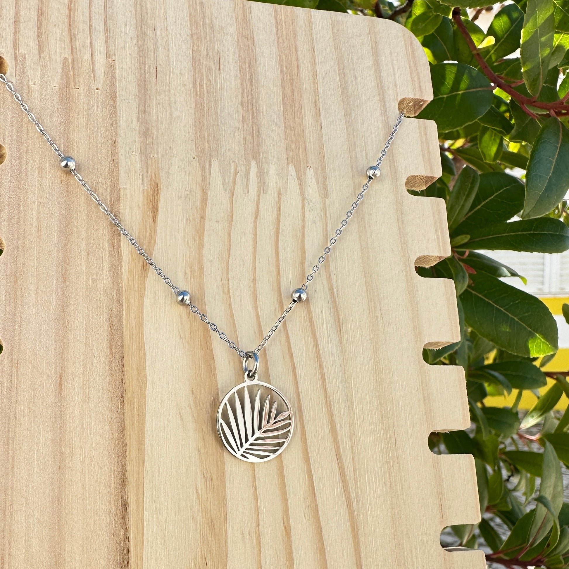 Silberne Edelstahl Kette mit rundem Palmblatt Motiv auf hellem Holzuntergrund.