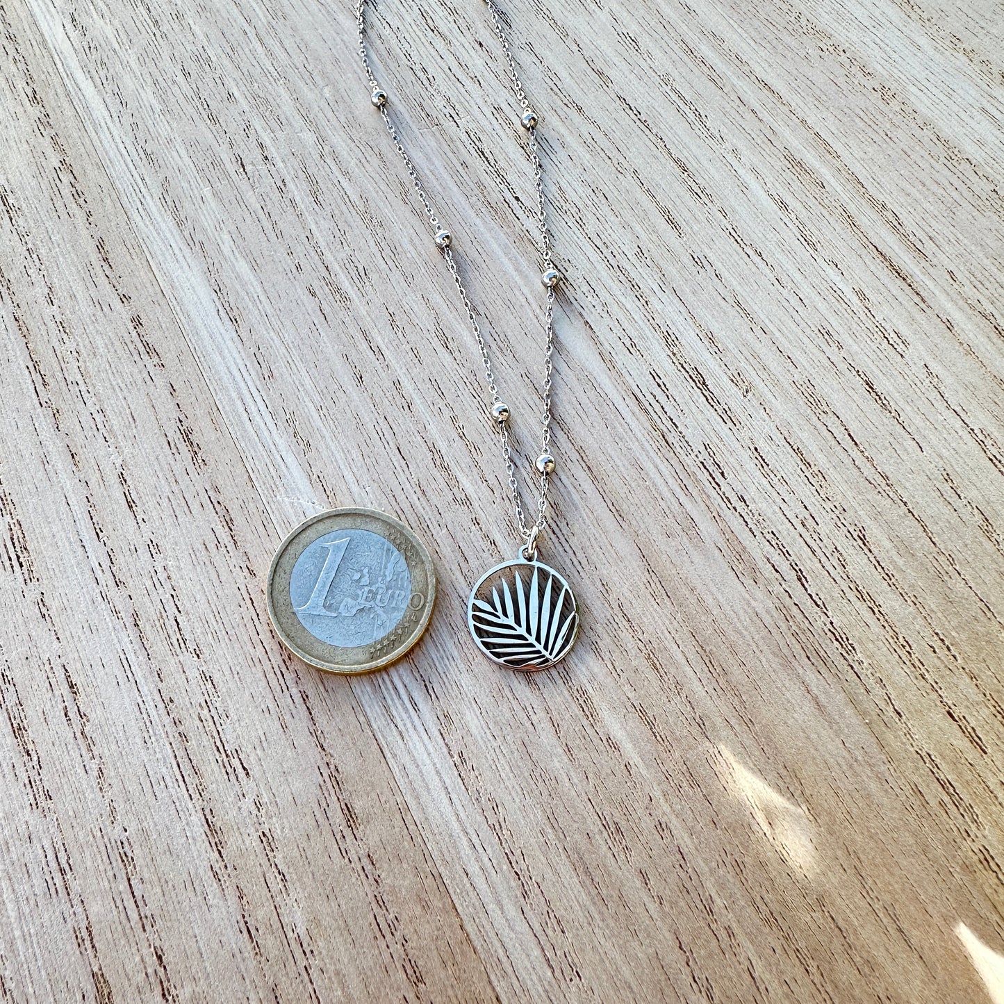 Silberne Palmblatt Halskette aus Edelstahl im Größenvergleich neben einer 1-Euro-Münze.