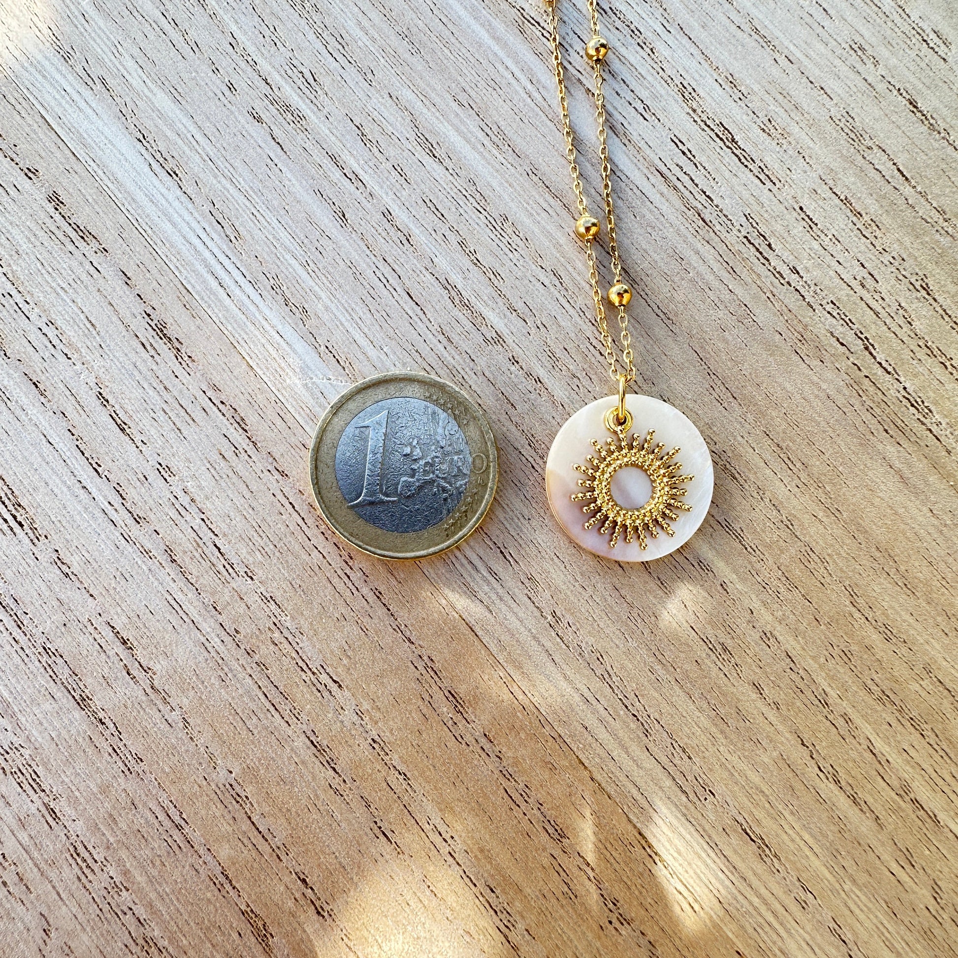 Goldene Sonnenkette mit Perlmutt Anhänger im Größenvergleich neben einer 1-Euro-Münze.