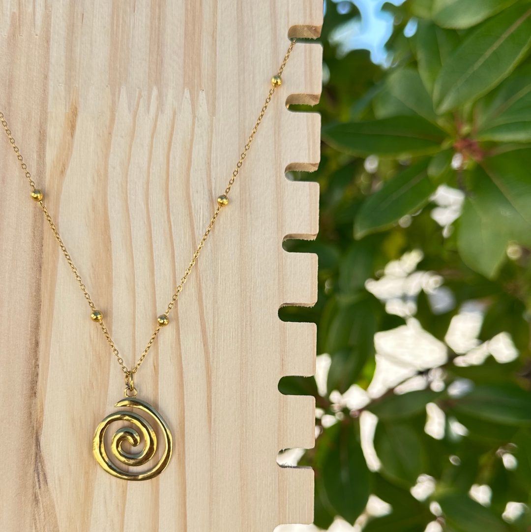 Goldene Edelstahl-Halskette mit Spiral-Anhänger auf Holzdisplay vor grünem Hintergrund