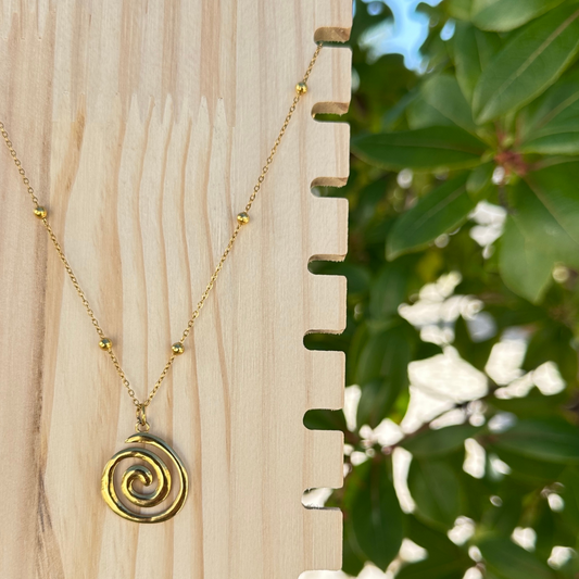 Goldene Edelstahl-Halskette mit Spiral-Anhänger auf Holzdisplay vor grünem Hintergrund