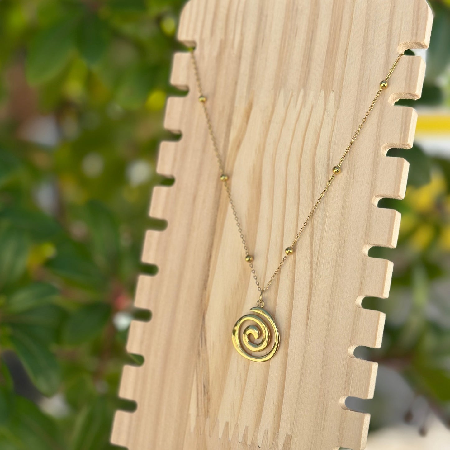 Spiral-Halskette in Gold aus Edelstahl, präsentiert auf Holzständer im natürlichen Außenlicht